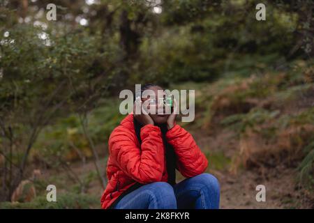 Giovane donna che indossa occhiali futuristici seduti nella foresta Foto Stock