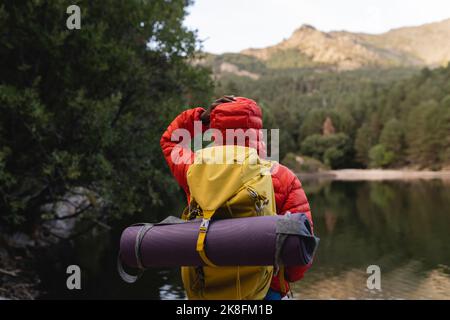 Giovane donna in piedi con zaino davanti al lago Foto Stock
