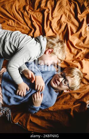 Felici fratelli che giocano e sdraiati a letto a casa Foto Stock