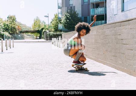 Giovane donna accovacciata sullo skateboard all'esterno dell'edificio Foto Stock