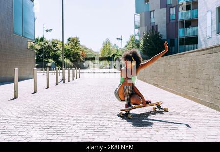 Donna accovacciata sullo skateboard all'esterno dell'edificio Foto Stock