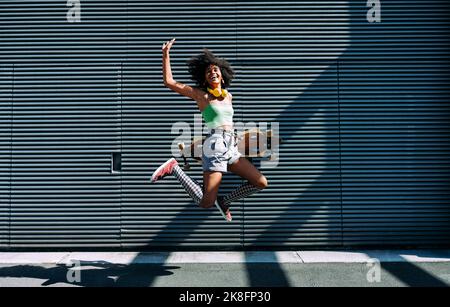 Giovane donna spensierata con skateboard che salta davanti al muro Foto Stock