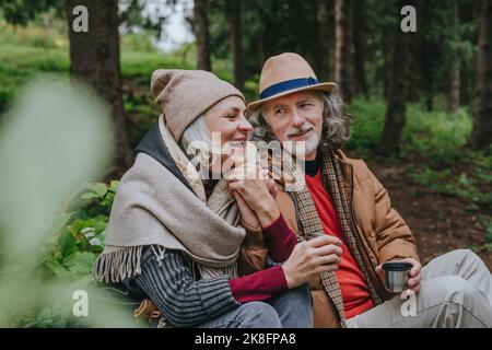 Donna matura sorridente con uomo anziano seduto nella foresta Foto Stock