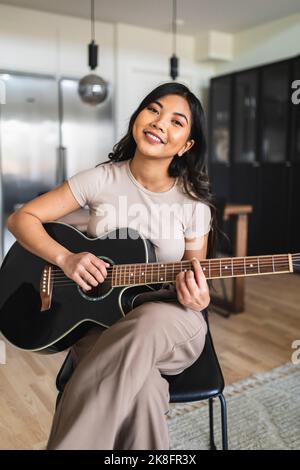 Donna sorridente a suonare la chitarra a casa Foto Stock