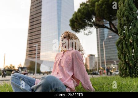 Donna sorridente che si rilassa sull'erba in città Foto Stock