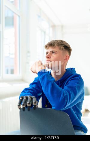 Ragazzo giovane e premuroso con un braccio amputato seduto sulla sedia Foto Stock