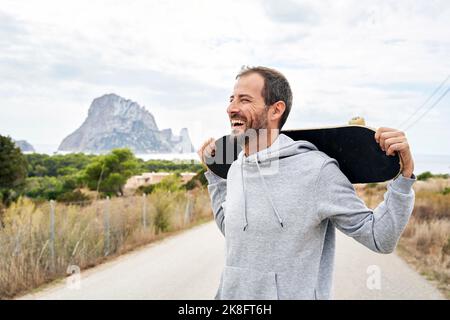 Uomo allegro che porta skateboard su strada Foto Stock