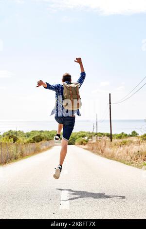 Backpacker con le braccia sollevate saltando su strada Foto Stock