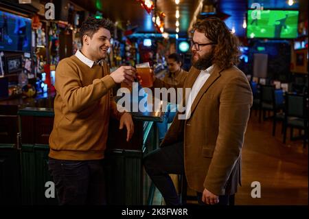 Happy amici maschi tintinnanti con boccali da birra in pub Foto Stock