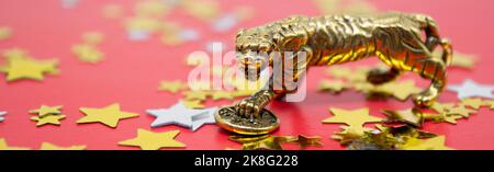 Banner con una figura in bronzo di una tigre con una moneta su sfondo rosso e stelle dorate, copia spazio. Foto Stock