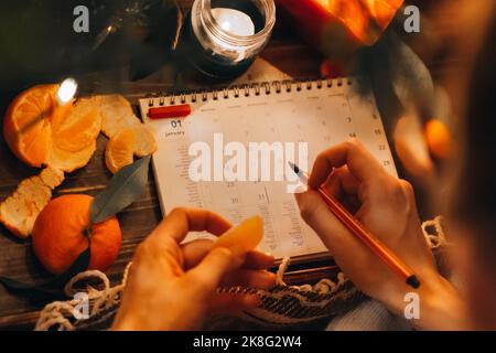 Pagina del pianificatore con i dolci di Natale, le arance del mandarino e la decorazione delle candele. Concetto di preparazione di Capodanno. Pianificazione del nuovo anno. Penna rossa per impugnare la mano femmina Foto Stock