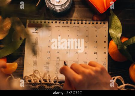 Pagina del pianificatore con i dolci di Natale, le arance del mandarino e la decorazione delle candele. Concetto di preparazione di Capodanno. Pianificazione del nuovo anno. Penna rossa per impugnare la mano femmina Foto Stock