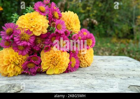 Su un tavolo di legno si trova un bouquet di fiori autunnali con dahlias gialle e astra rosa Foto Stock