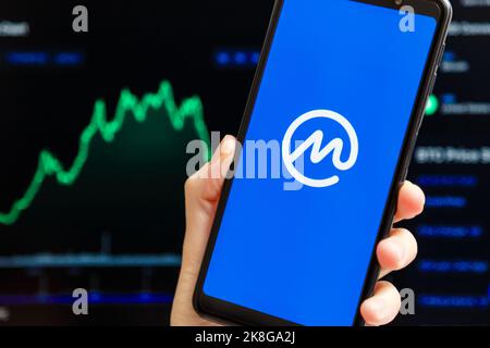 Ucraina, Odessa - Ottobre, 9 2021: Tenere a mano mobile con l'app CoinMarketCap in esecuzione sullo schermo dello smartphone, trading candelabro grafico in background. L'autorità di crittografia dei dati più affidabile al mondo Foto Stock