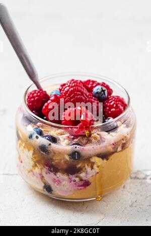 Farina d'avena durante la notte con bacche, burro di arachidi e sciroppo d'acero in vaso. Concetto di colazione vegana sana. Foto Stock