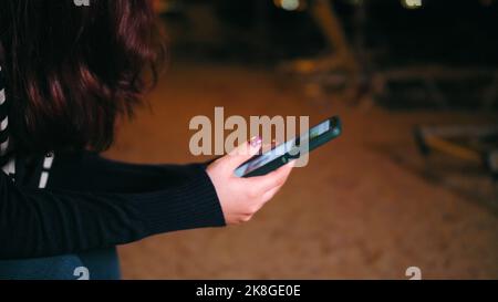 Primo piano giovane donna che flipping attraverso Telefono sfondo Spiaggia Notte Foto Stock