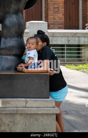 Medellin, Antioquia, Colombia - Settembre 12 2022: Giovane donna dei capelli neri tiene un bambino su una scultura del bronzo, la statua di un grande carattere femminile b Foto Stock