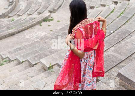 Dall'alto, vista posteriore di una giovane etnia femminile in un abito tradizionale che cammina al piano di sotto mentre esplora il luogo storico Foto Stock