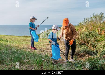 Pulire i volontari raccogliendo rifiuti in sacchi di rifiuti con bastoni su terreno erboso durante la campagna ambientale in campagna Foto Stock