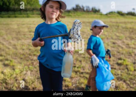 Pretenga i volontari in magliette blu e cappellini in piedi con le pinze del thrash e sacchetto del bidone mentre raccoglie i rifiuti di plastica sul prato erboso Foto Stock