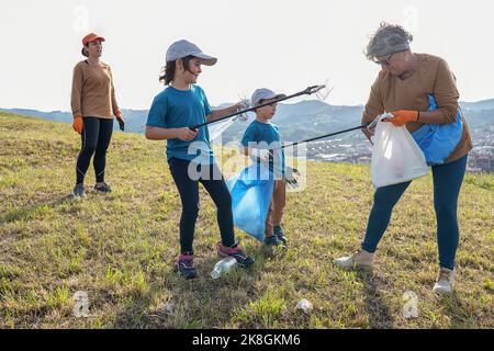 Pulire i volontari raccogliendo rifiuti in sacchi di rifiuti con bastoni su terreno erboso durante la campagna ambientale in campagna Foto Stock