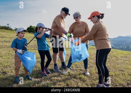 Pulire i volontari raccogliendo rifiuti in sacchi di rifiuti con bastoni su terreno erboso durante la campagna ambientale in campagna Foto Stock