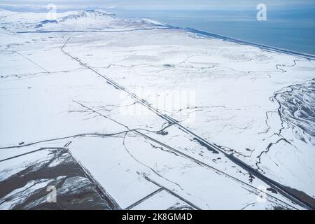 Vista del drone del fiume e della montagna innevata situata sulla riva del mare contro il cielo in una giornata invernale tempestosa in Islanda Foto Stock