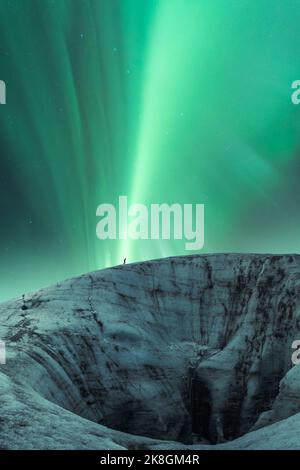 Formazione irregolare di ghiaccio del ghiacciaio Vatnajokull con turista situato contro il cielo notturno con verde brillante aurora borealis il giorno d'inverno in Islanda Foto Stock