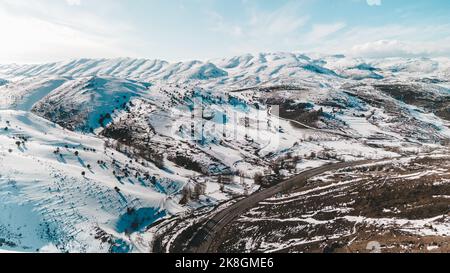 Vista mozzafiato del drone di strada asfaltata che va nella valle vicino alle piste di montagne innevate nella fredda giornata invernale in Turchia Foto Stock