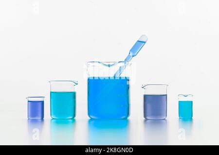 Raccolta di fiasche da laboratorio in vetro di varie dimensioni e forme riempite con liquido blu brillante poste su superficie bianca in studio Foto Stock