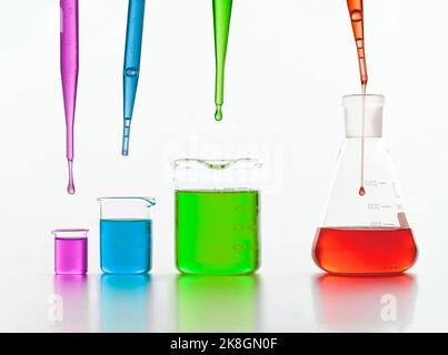 Set di fiasche chimiche di varie dimensioni con liquidi colorati poste sul tavolo su sfondo bianco in laboratorio Foto Stock