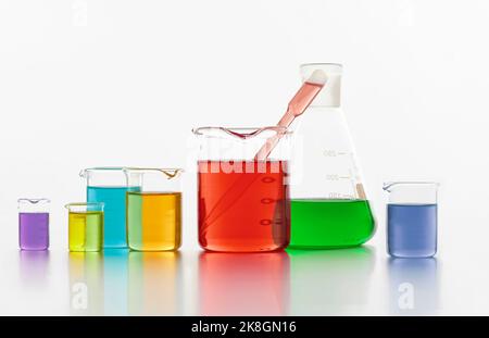 Set di fiasche chimiche di varie dimensioni con liquidi colorati poste sul tavolo su sfondo bianco in laboratorio Foto Stock