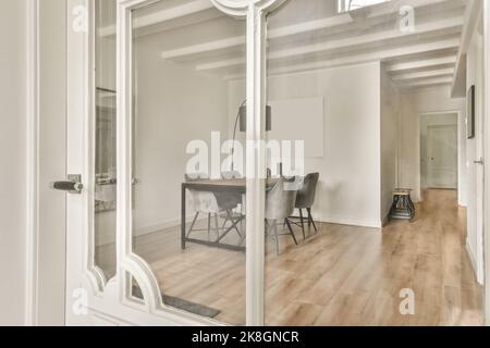 Interni di moderno stile minimalista sala da pranzo con tavolo in legno e sedie grigie situate sotto lampade vicino a porta di vetro di giorno Foto Stock