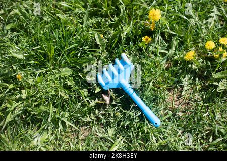 Rastrello per bambini sull'erba. Giocattolo dimenticato dal bambino. Strumento da giardino blu su prato. Foto Stock