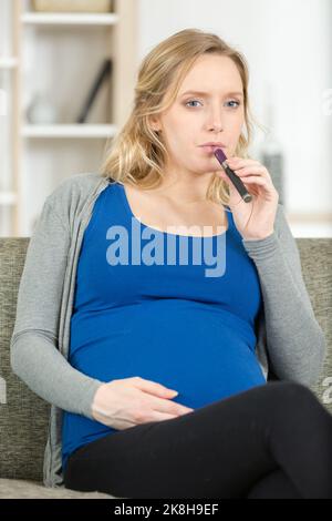 affascinante donna incinta che fuma una sigaretta elettronica Foto Stock