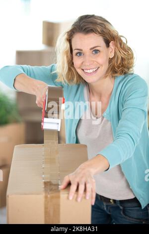 donna felice sigillando con nastro grande scatola di cartone Foto Stock