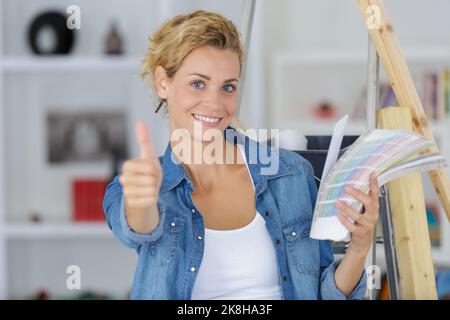 donna che tiene grafici a colori della vernice che fanno i pollici-in su il gesto Foto Stock