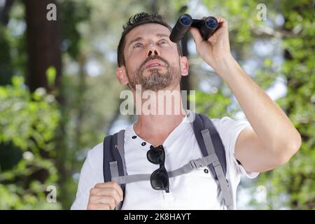 uomo con binocoli in piedi nei boschi Foto Stock