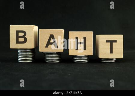 Concetto di indebolimento del baht thailandese, deprezzamento del valore e svalutazione. Diminuzione della pila di monete su sfondo nero scuro. Foto Stock