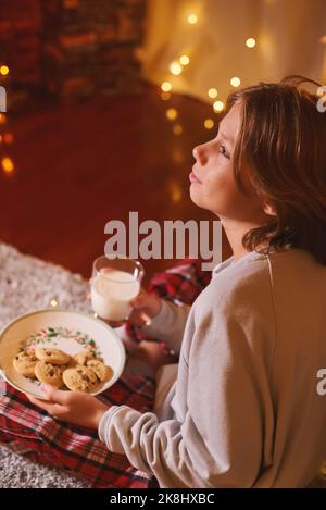 Carino ragazzo pronto per Babbo Natale in attesa con biscotti e latte. Credenza nella fiaba Foto Stock