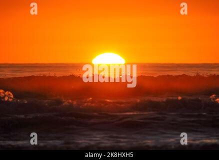 Il sole scende dietro le onde Foto Stock
