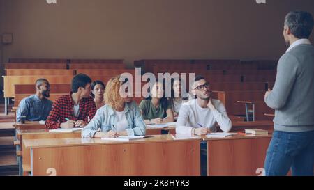 Il tutor emotivo parla con gli studenti adulti spiegando nuove informazioni mentre gli studenti attenti ascoltano e prendono appunti. Professione, istruzione superiore e concetto di persone. Foto Stock