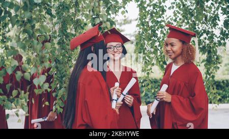 Tre graziose ragazze laureate stanno parlando e tenendo i diplomi il giorno della laurea, gli studenti sono orgogliosi ed eccitati. Conversazione, educazione e concetto di successo per i giovani. Foto Stock
