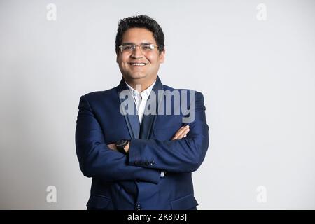 Ritratto di un giovane uomo d'affari indiano sicuro in un vestito in piedi con la sua croce delle braccia, isolato su sfondo bianco studio Foto Stock