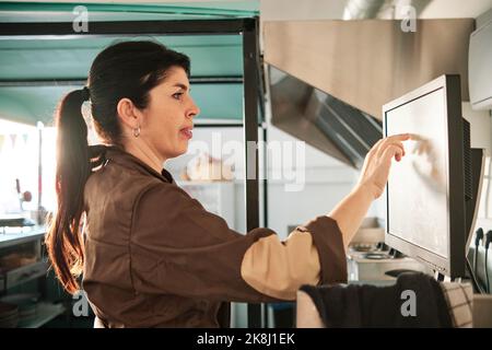 Donna che controlla gli ordini su un touch screen mentre lavora in un ristorante. Foto Stock