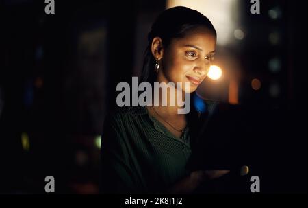 Navigare nel mondo digitale di notte. Una giovane donna d'affari che usa un tablet digitale in un ufficio di notte. Foto Stock