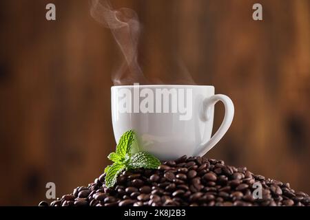 Ricco e aromatico. Colpo di primo piano di una foglia di menta e una tazza su un mucchio di chicchi di caffè. Foto Stock