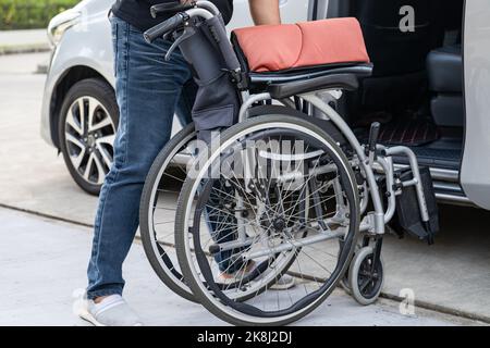 Donna asiatica pieghevole e sollevare la sedia a rotelle nella sua auto. Concetto di accessibilità. Foto Stock