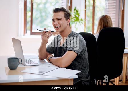 Registrazione di una nota vocale da inviare a un cliente. Un giovane uomo d'affari che utilizza un cellulare mentre lavora in ufficio. Foto Stock