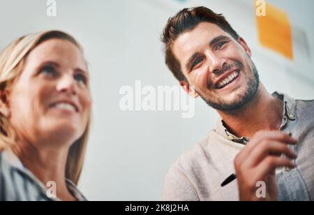 Theyre pieno di idee. Due colleghi d'affari brainstorming su una lavagna di vetro nel loro ufficio. Foto Stock